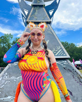 festival-goer embodies vibrant festival spirit in her rave outfits. wearing a patterned desert themed bodysuit, while rocking a colorful psychedelic accessories