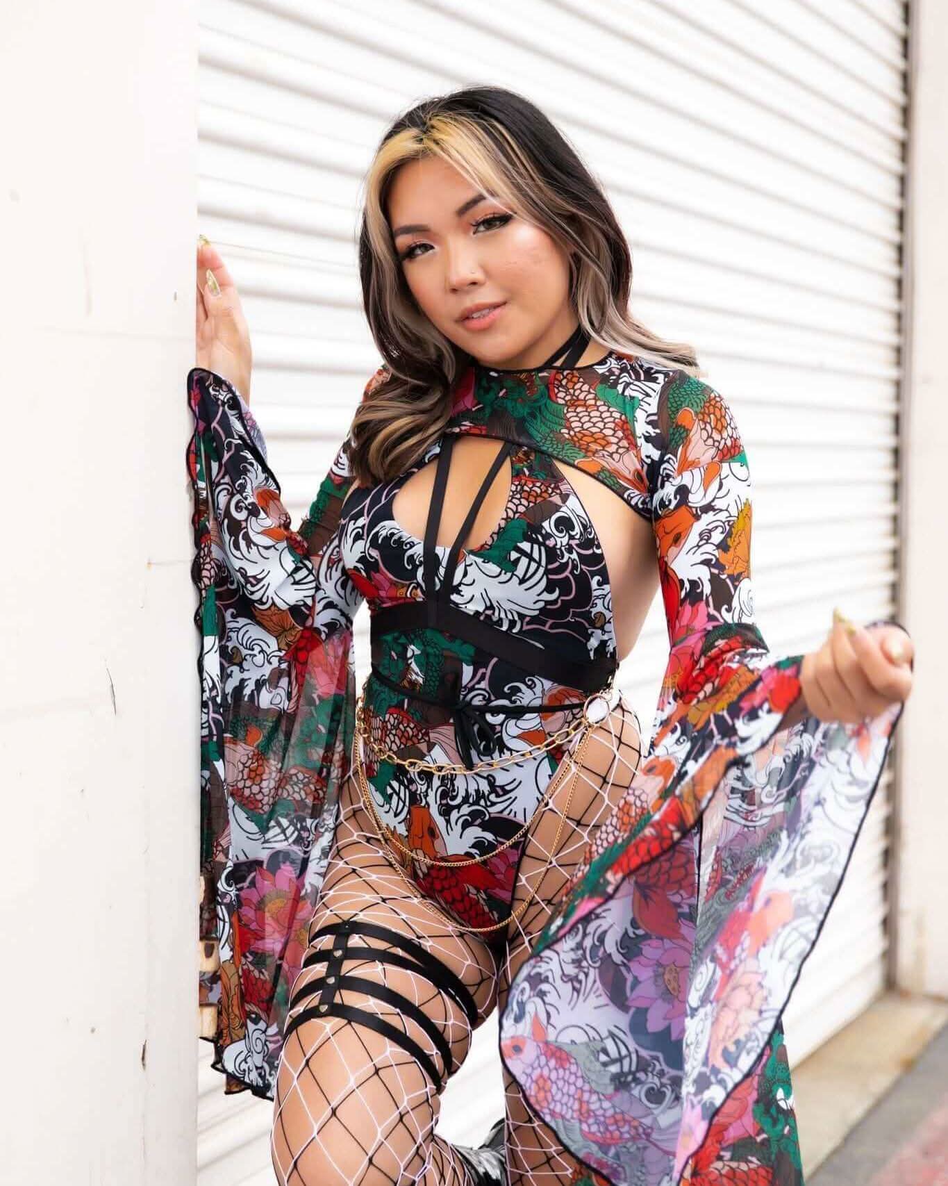 Woman in colorful festival outfit with floral designs, posing in a trendy mesh look against a white background.
