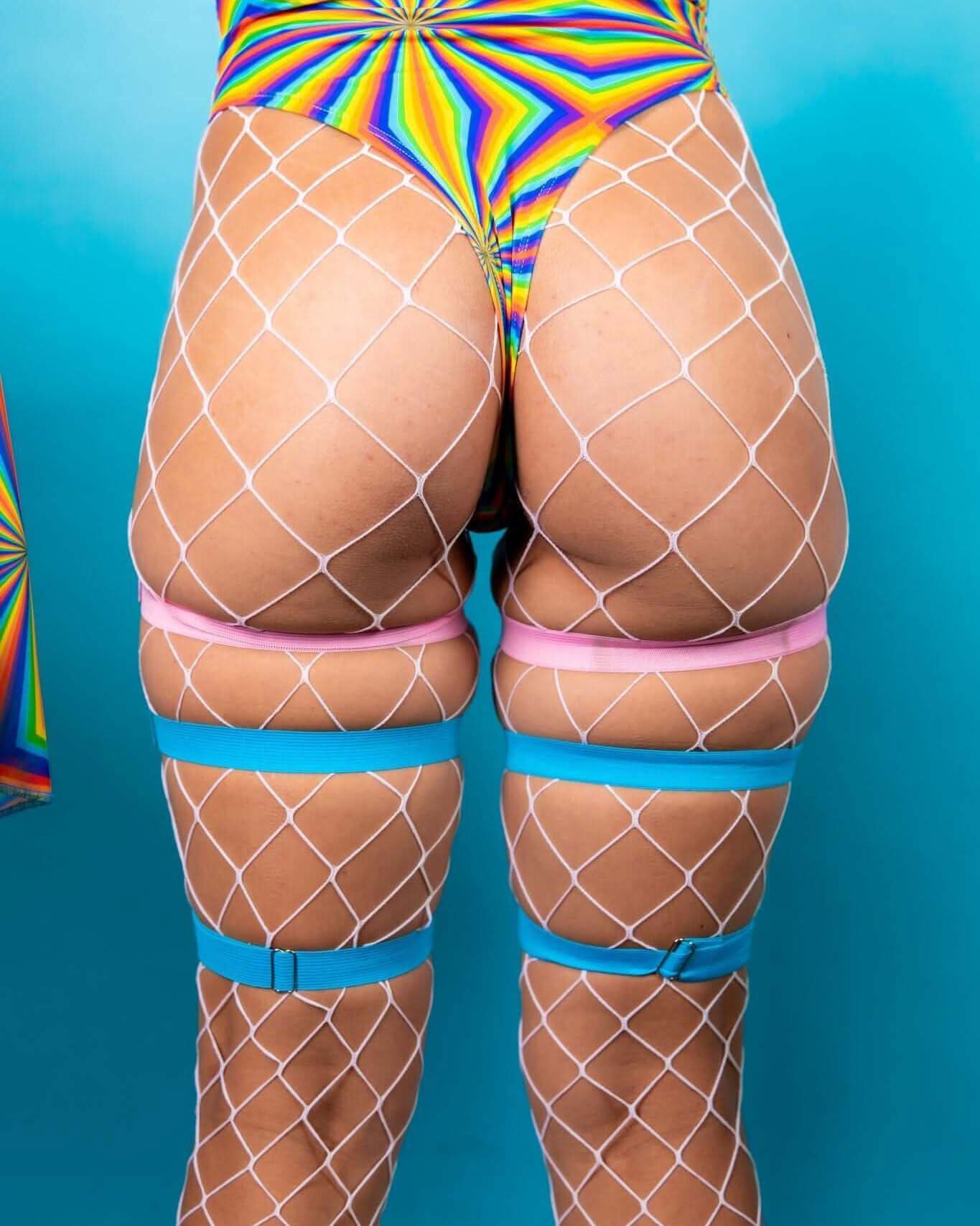 Model showcasing colorful fishnet tights with pink and blue leg garters, perfect for rave outfits and festivals.