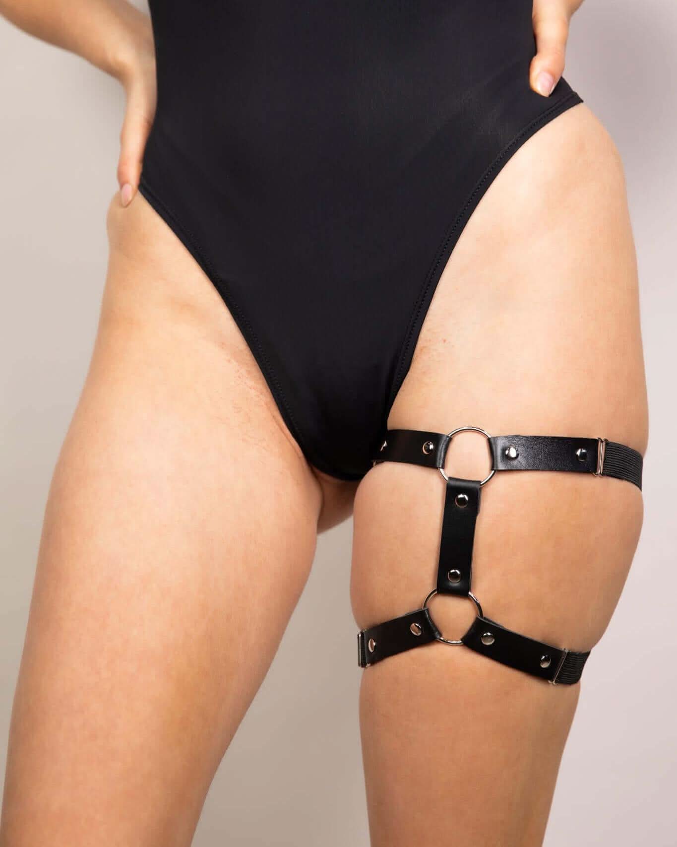 Black leather adjustable leg garter worn with a sleek black bodysuit, perfect for edgy rave outfits.