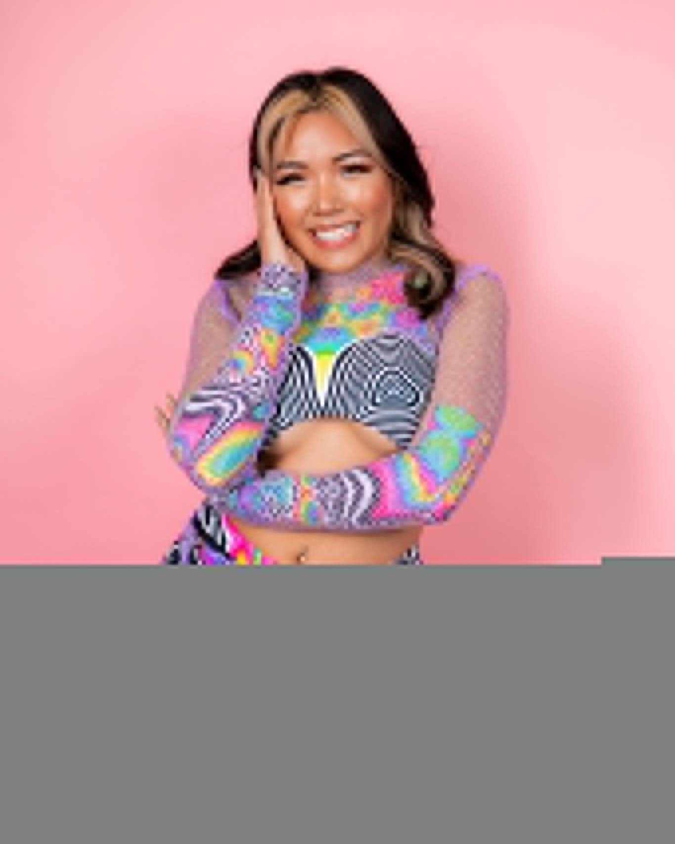 Smiling woman in colorful rave outfit with long sleeves, posing against a pink background. Perfect for festival fashion.
