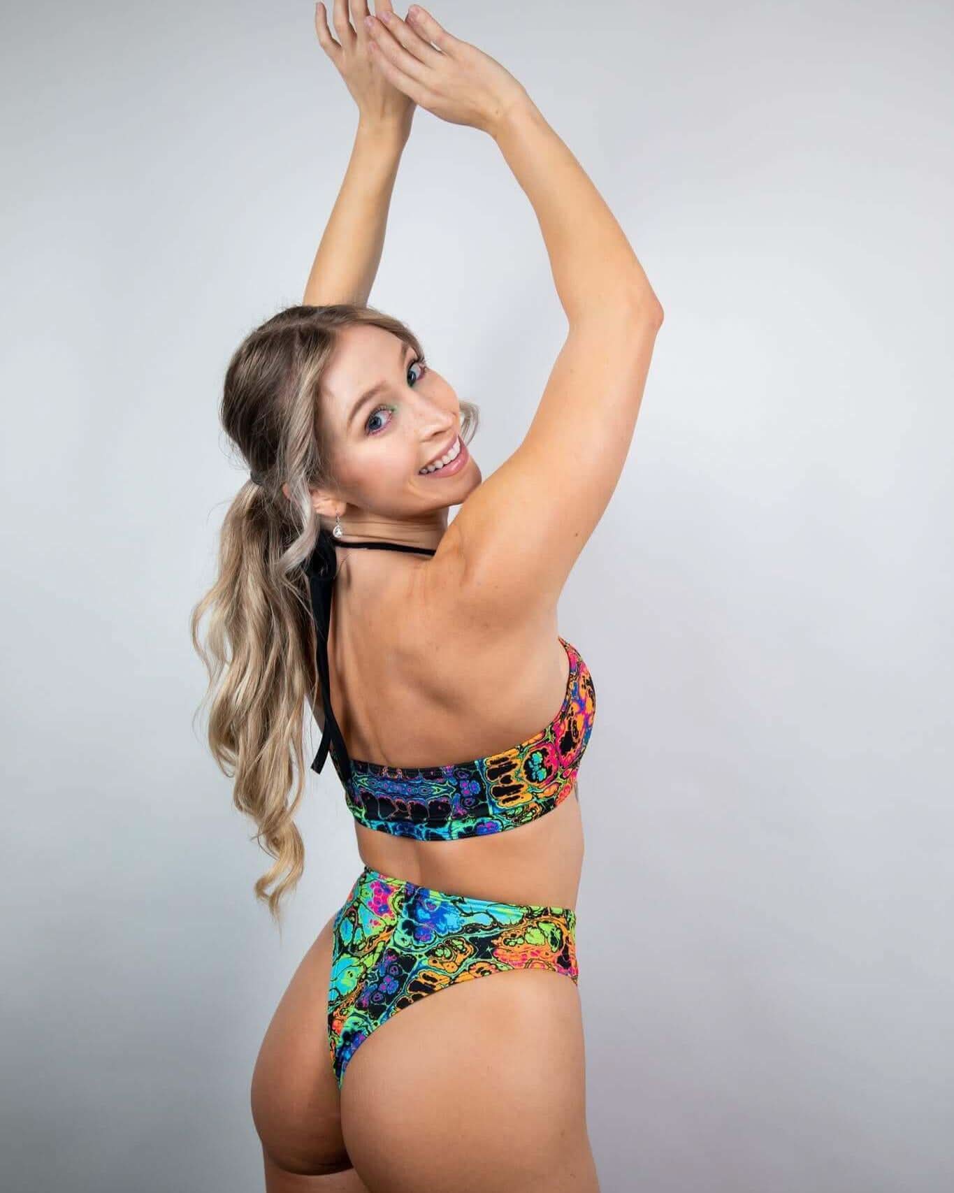 Model showcasing the Lucidity High Waisted Thong in a vibrant psychedelic rainbow design, ideal for rave outfits.