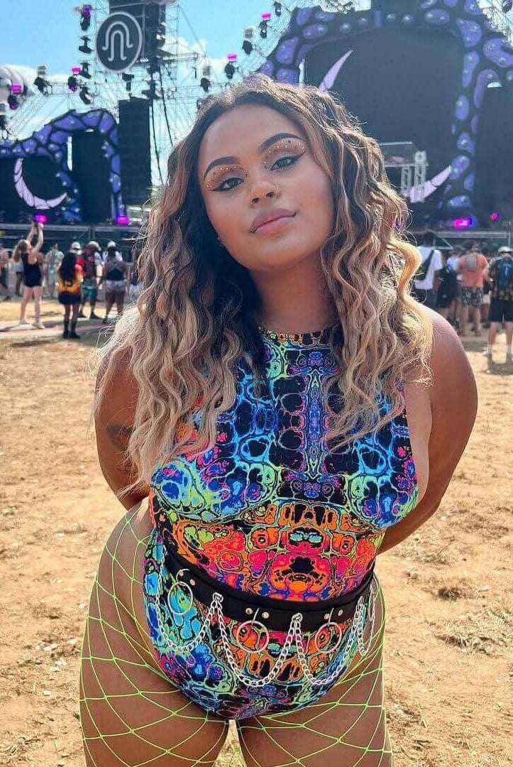 Model wearing the Lucidity Sideboob Bodysuit with colorful psychedelic print at a rave festival.
