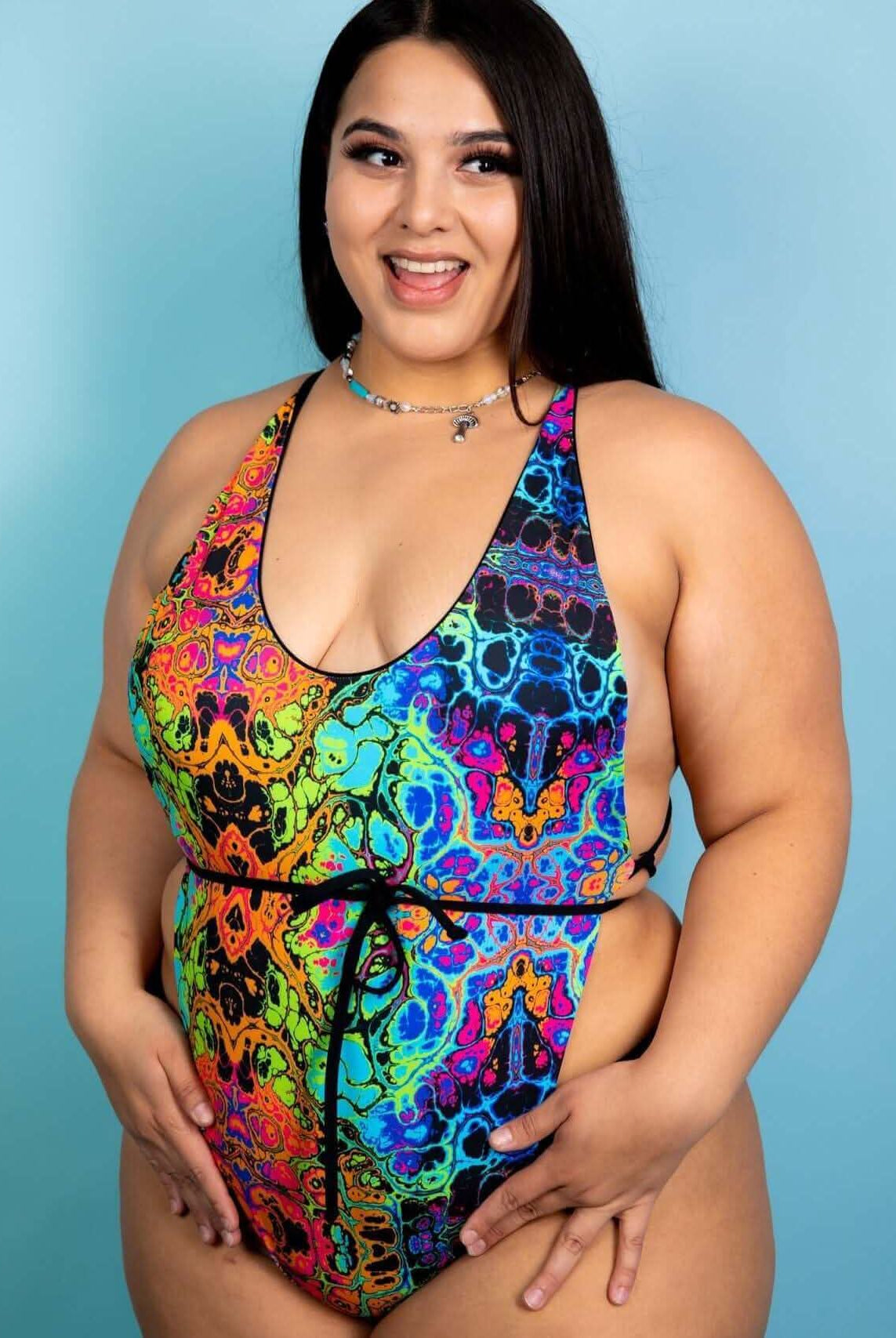 Plus-size model showcasing the Lucidity Temptation Cheeky One Piece, a vibrant rainbow rave outfit perfect for festivals.