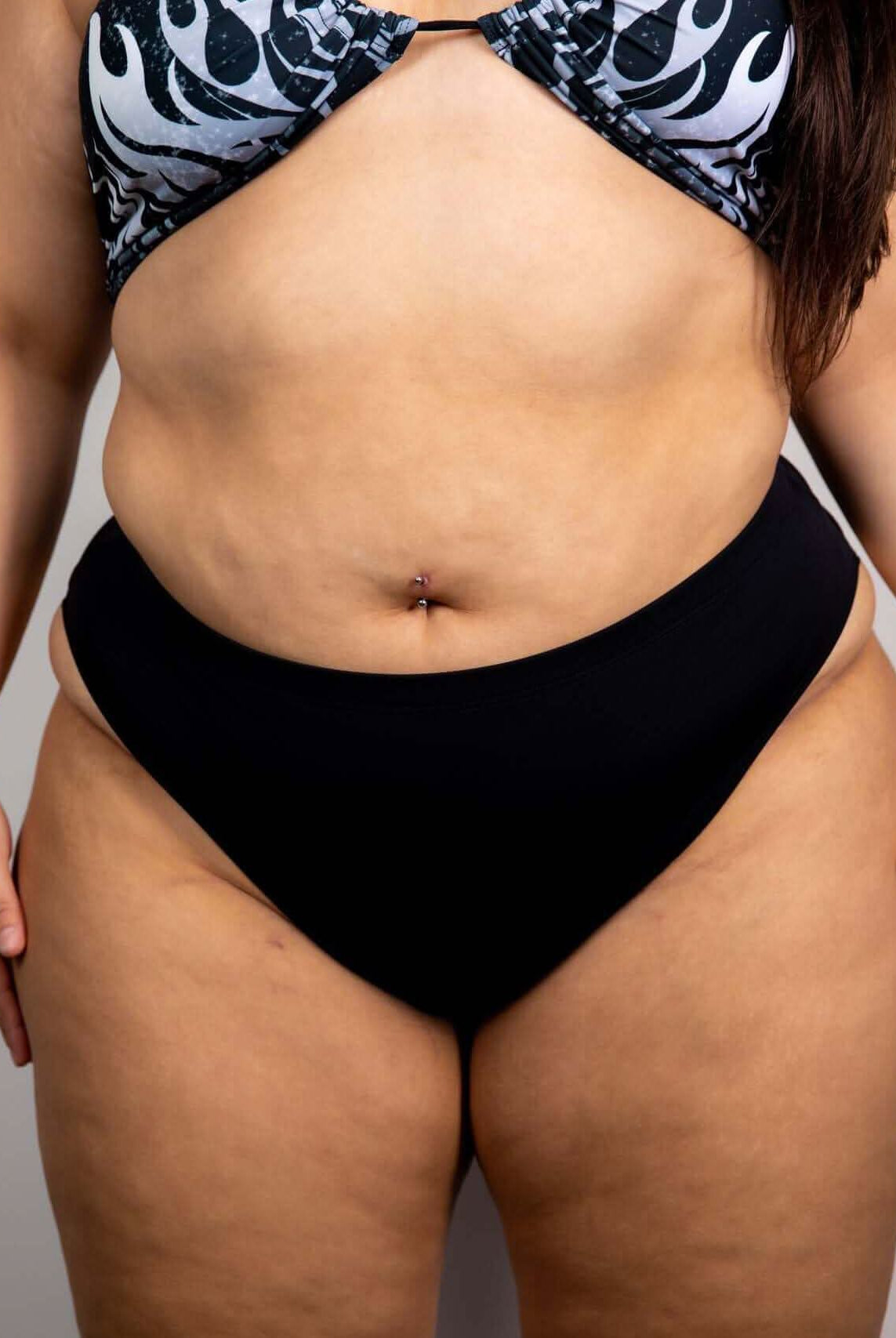 High-waisted black Brazilian bottoms showcased with a colorful flame-patterned bikini top, perfect for rave outfits.