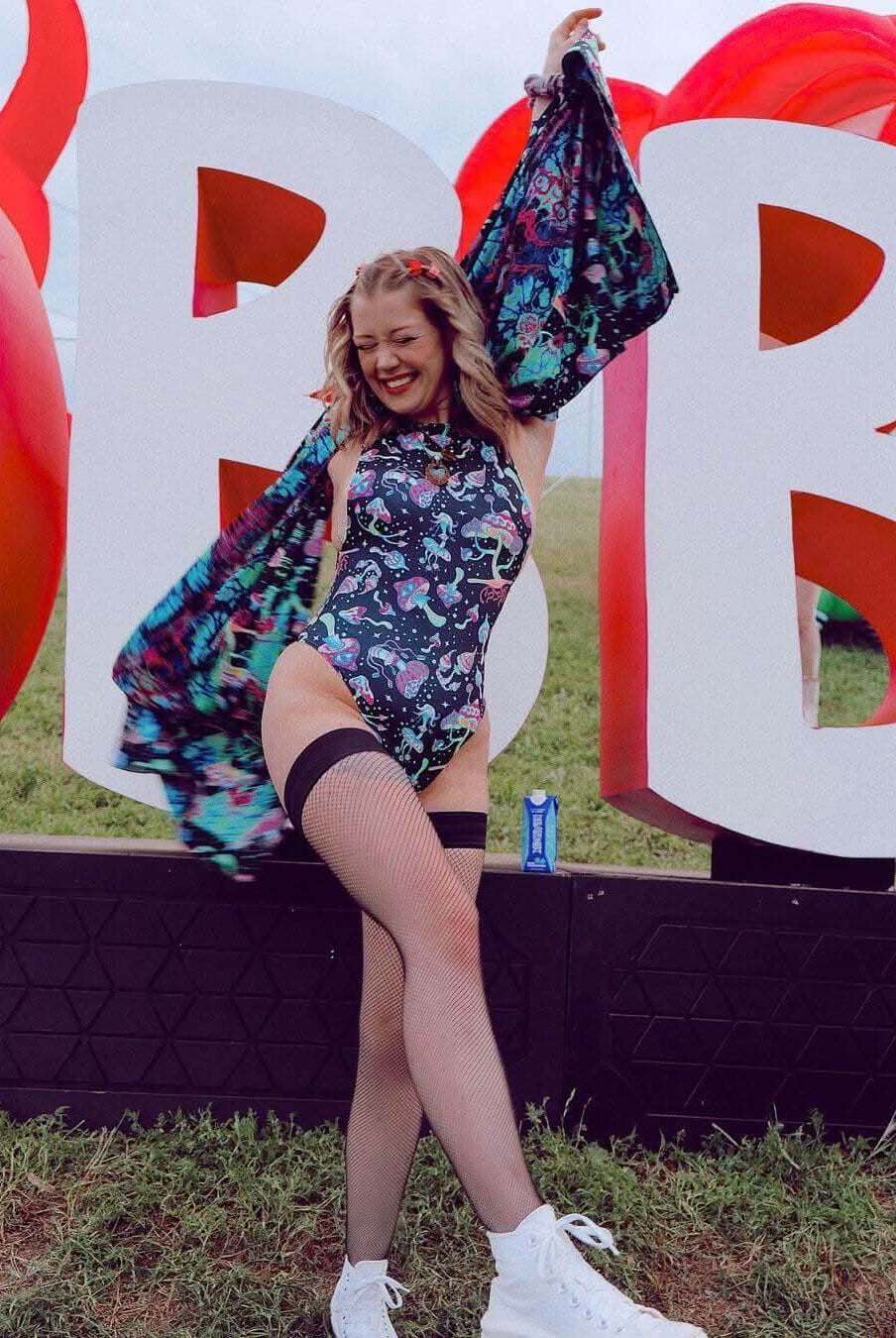 Young woman in a psychedelic mushroom bodysuit posing joyfully at a festival, showcasing vibrant rave outfit style.