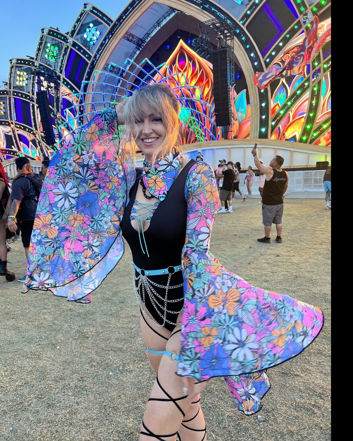 Alyssa in front of a festival main stage, wearing a black bodysuit with floral mesh bell sleeves