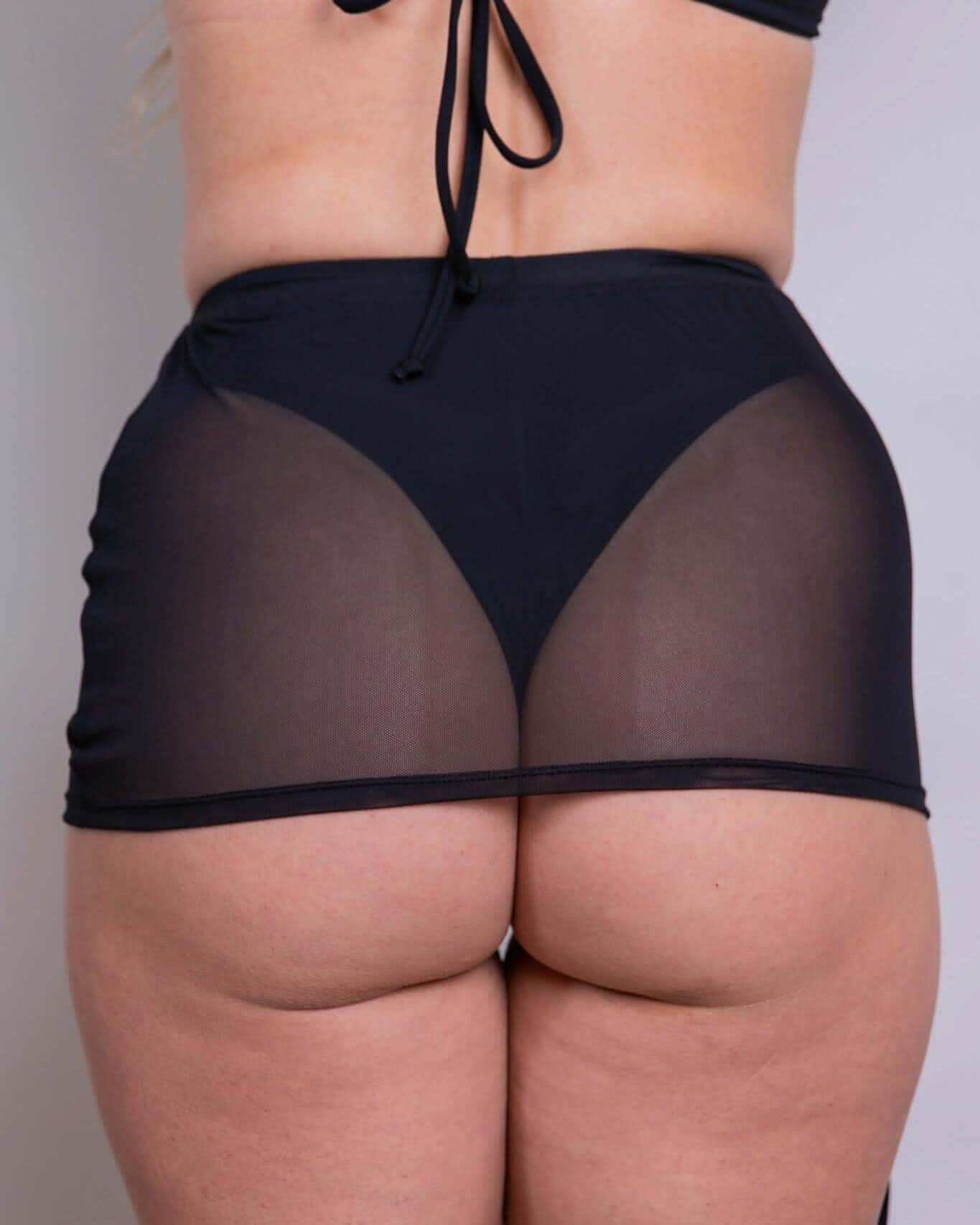 Back view of black mesh cinch rave skirt with adjustable drawstring worn by model against white background
