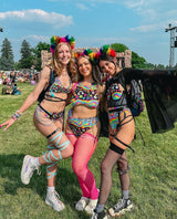 ravers in rainbow rave outfits stand in front of a music festival stage