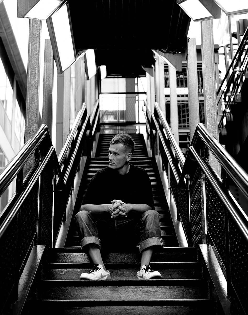 KASKADE ANNOUNCES NEW ALBUM UNDUX. Black and white image of artist sitting on stairs.