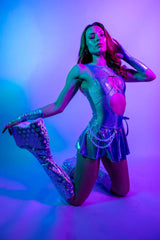 Model in a shimmering silver rave outfit with colorful lighting, showcasing a glamorous party style.