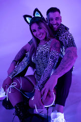 A stylish couple wearing vibrant rave outfits with glowing elements, set against a purple background.
