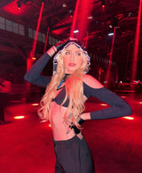 rave girl stands in dark techno club with red lighting in a black cutout outfit and hood