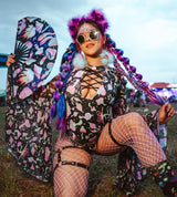 rave girl in purple and black mushroom outfit with matching braids and accessories poses holding a mushroom fan in a festival crowd