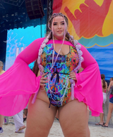 rave girl in bright rainbow trippy rave outfit with pink mesh bell sleeves stands in front of a stage