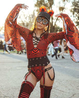 A festival-goer in a striking red rave bodysuit poses confidently. She wears a lace-up front bodysuit with matching accessories, thigh-high stockings, and unique sunglasses, set against an outdoor festival backdrop