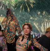 rave girl in orange and blue rave outfit with bell sleeves stands in front of the edc fireworks