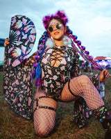 excited rave girl in a purple mushroom rave outfit with matching fan and purple fluffy ears and braids kneels in festival grounds