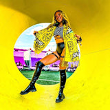 Woman in stylish rave outfit poses with a vibrant scarf in a colorful festival setting.