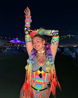 excited raver in rainbow rave outfit and accessories smiles with the festival lights behind her