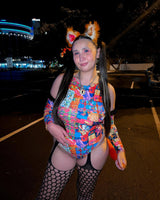raver in a patchwork colorful rave outfit with matching fluffy ears and black tights stands in front of event venue