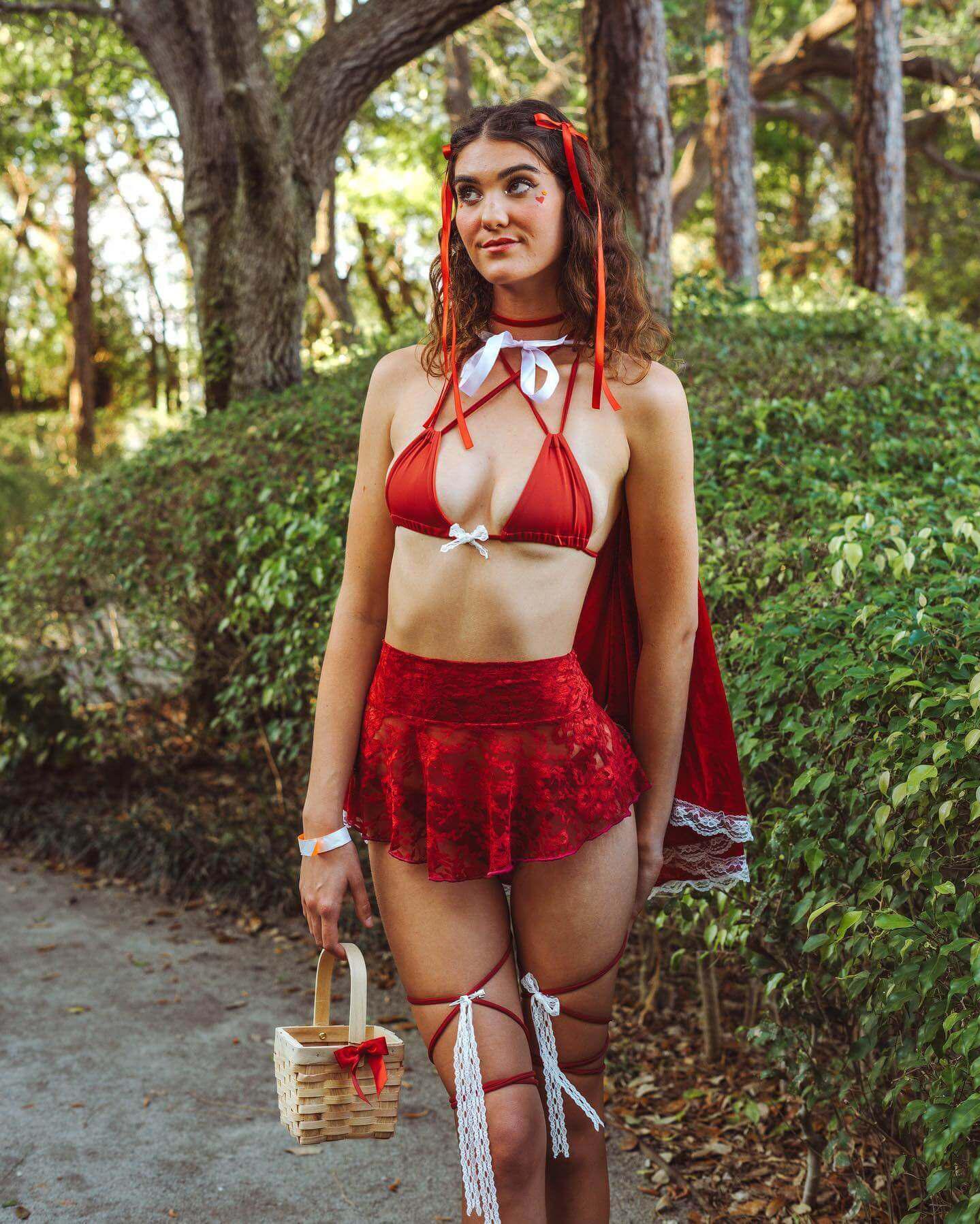 Model wearing a red lace micro skater skirt with a matching top and cape, styled for a whimsical outdoor setting.