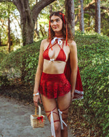 rave girl in a scarlet lace detailed outfit with white bow stands in a forest backdrop