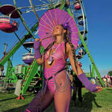 Young woman in a vibrant rave outfit with a purple parasol, posing near a colorful Ferris wheel at an outdoor festival.