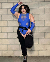 Confident woman in a blue cut-out bodysuit and thigh-high boots strikes a pose against a concrete wall, showcasing her curves