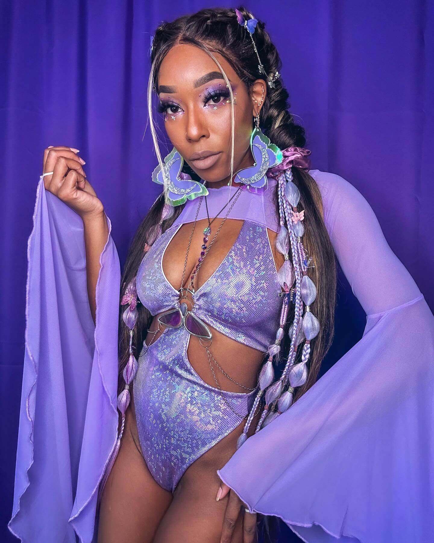Poc rave girl poses with a mystical aura in a sparkling lilac rave set, complemented by lavender backdrop