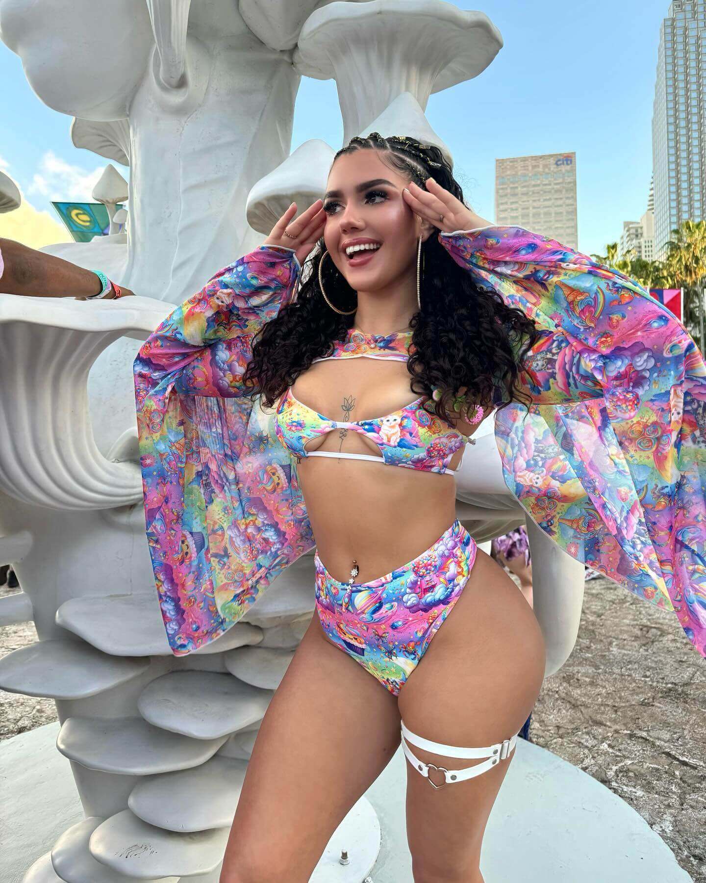 A woman wearing a rainbow bikini and matching bell sleeves. She is posing at a music festival.