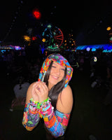 A girl at a music festival wearing a rainbow patchwork hood with matching arm sleeves.
