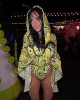 rave girl in a yellow patterned hooded rave outfit with glitter makeup stands at a festive nighttime event