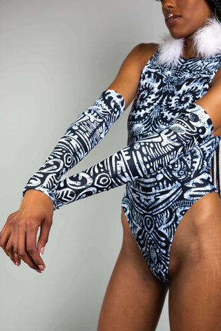 An up-close photo of the side of a girl wearing black and white tribal printed arm sleeves and a matching bodysuit.