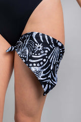 An up close photo of a girl's leg with a black and white printed tribal bandana tied around it.