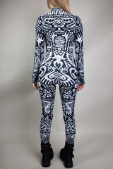 A blonde girl wearing a black and white tribal printed catsuit, with long sleeves and long pants. She is facing away from the camera.