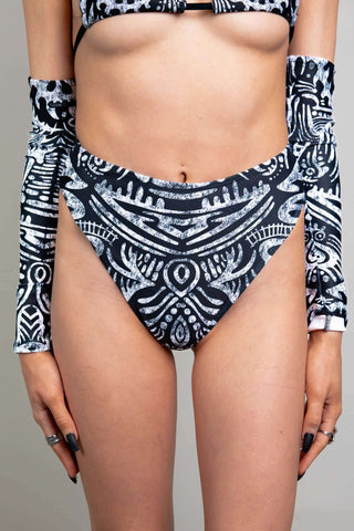 An up close photo of a girl wearing black and white printed rave bottoms that resemble a high waisted bikini bottom.