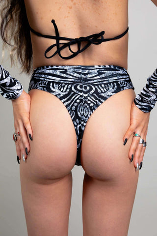 An up close photo of a girl wearing black and white printed rave bottoms that resemble a high waisted bikini bottom. She is facing away from the camera.