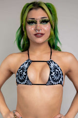 A photo of a girl with green hair wearing a black and white tribal printed bikini top with a strap across the front.