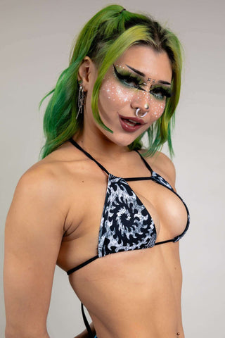 A photo of a girl with green hair wearing a black and white tribal printed bikini top with a strap across the front.
