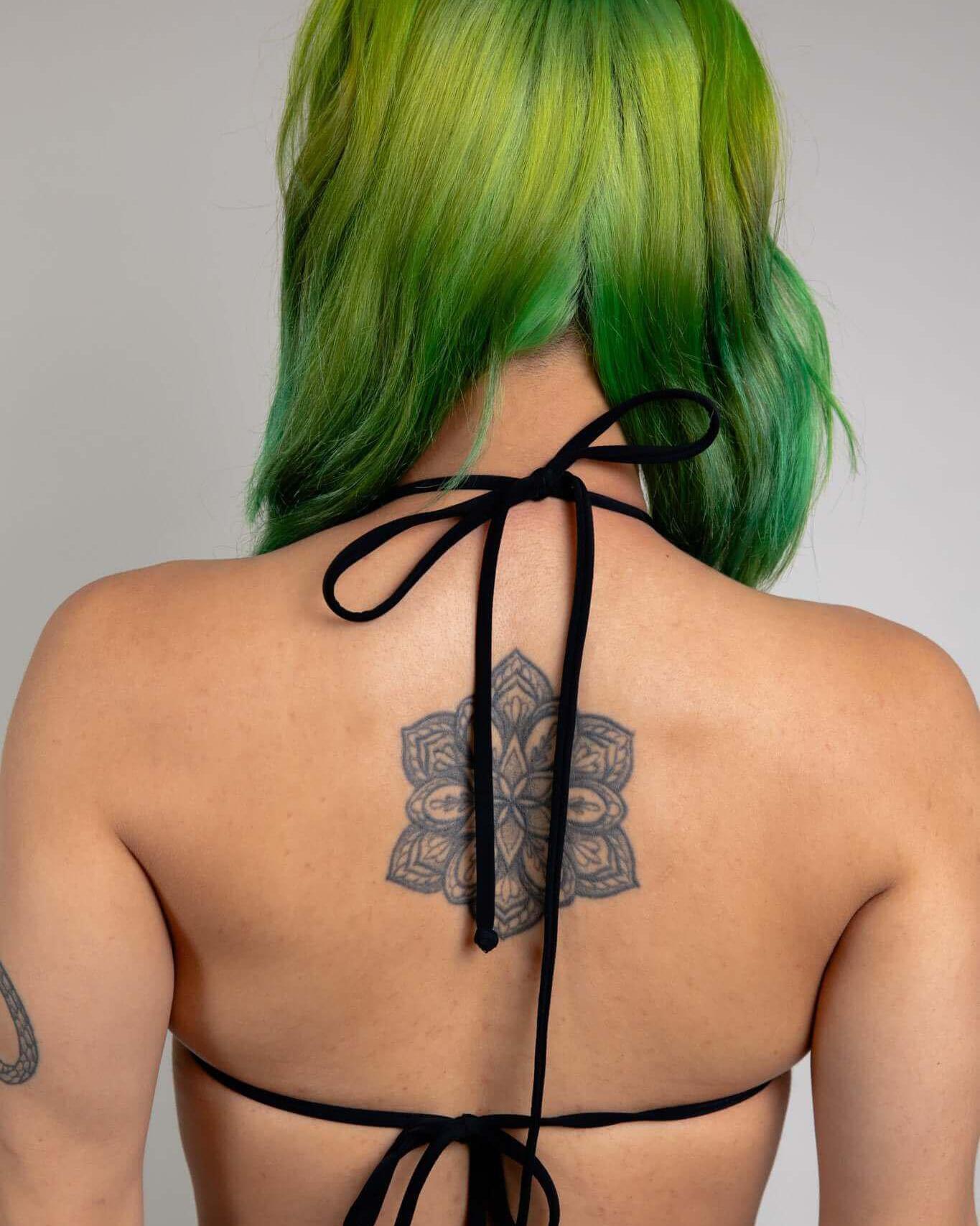 Back view of a woman in an Archaic Strappy Bikini Top, showcasing long straps and green hair with a tattoo.