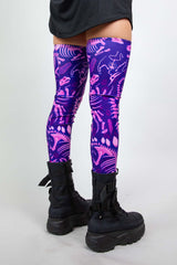 Model wearing Freedom Rave Wear thigh-high leg sleeves with purple dinosaur print and black boots, shown from the side, ideal for raves.