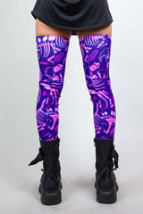 Model wearing Freedom Rave Wear thigh-high leg sleeves with purple dinosaur print and black boots, shown from the back, ideal for raves.