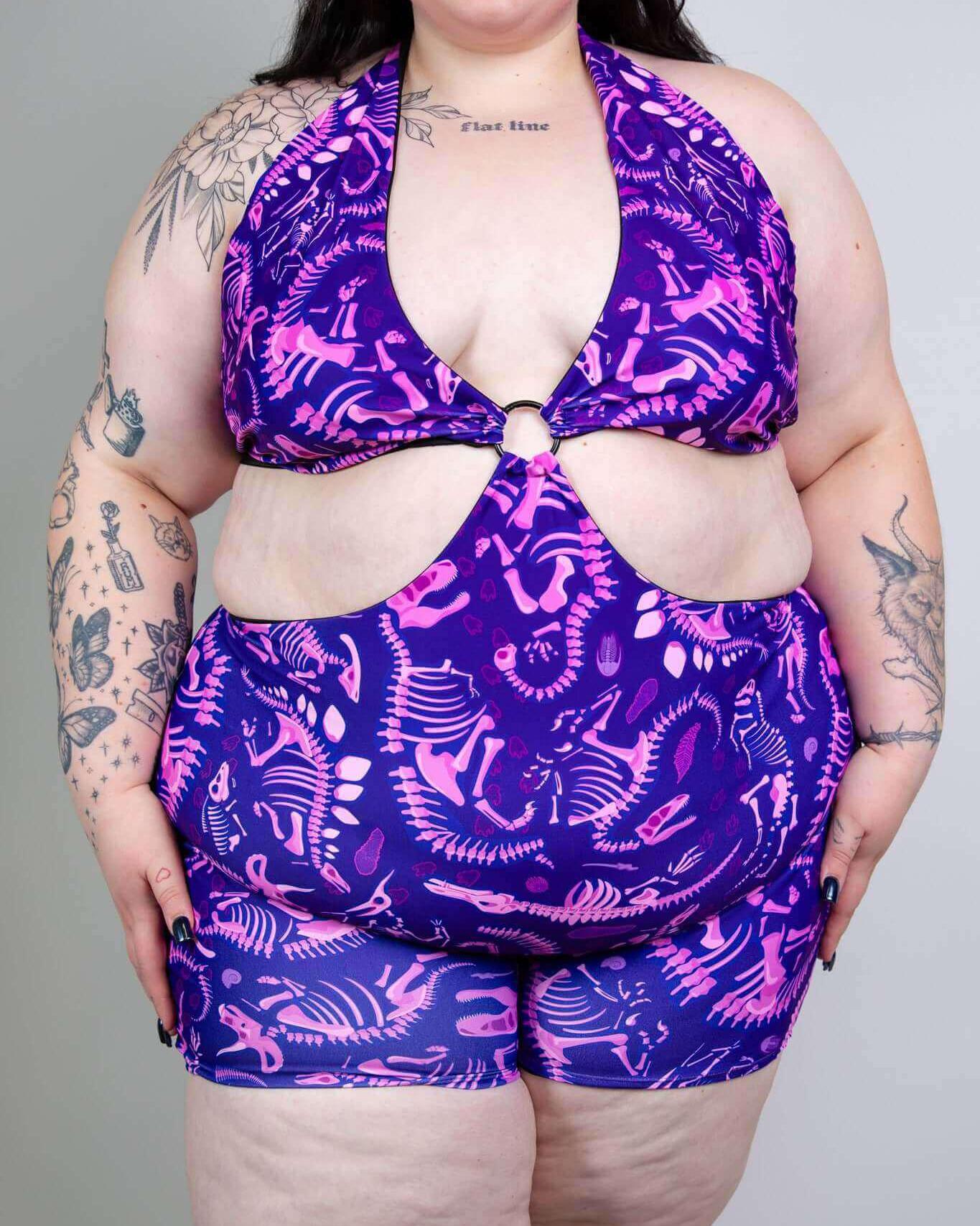 Plus-size model in purple dino fossil rave outfit, showcasing playful design and vibrant colors, perfect for summer fun.