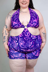 Plus-size model in purple dino fossil rave outfit, showcasing playful design and vibrant colors, perfect for summer fun.