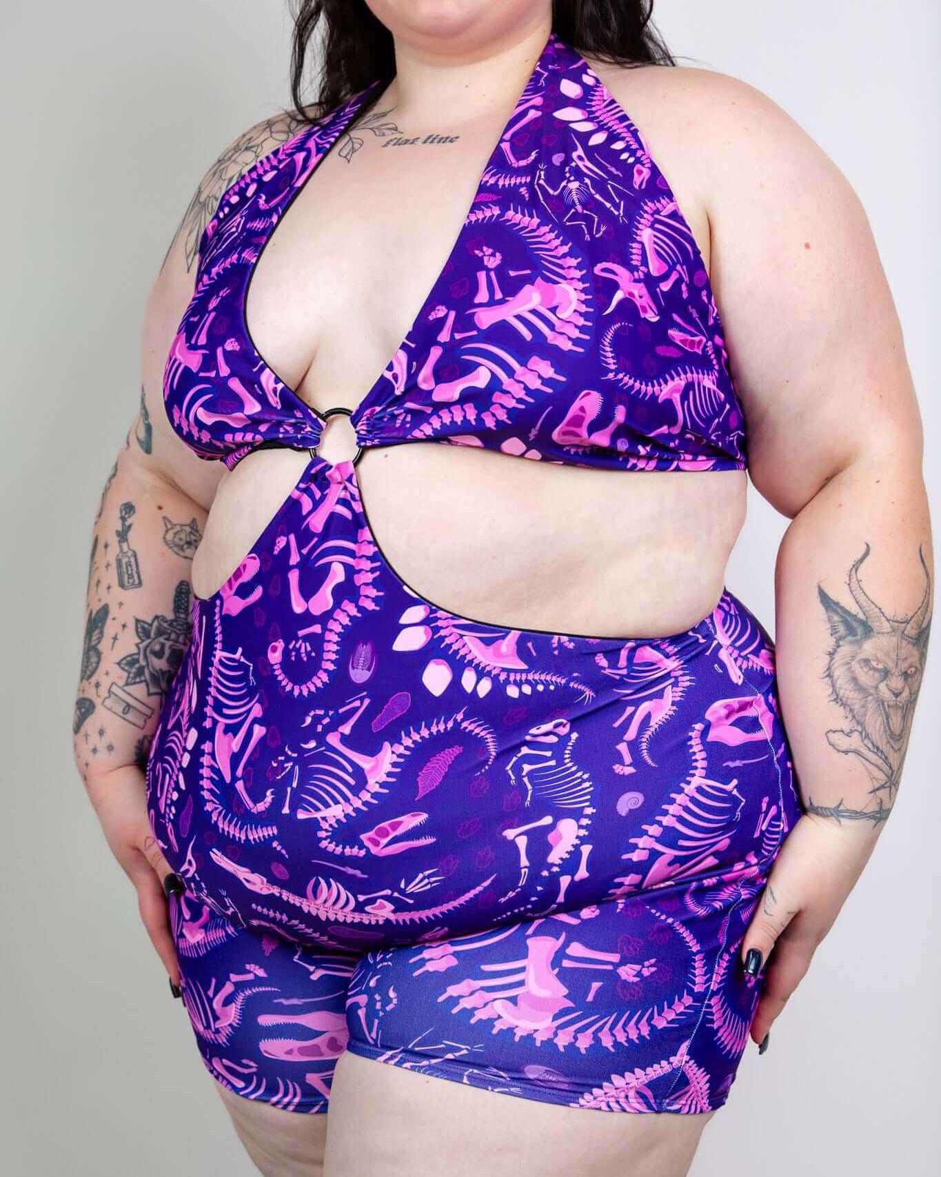 Playful purple dinosaur fossil swimsuit with cutout design, perfect for summer fun and rave outfits.