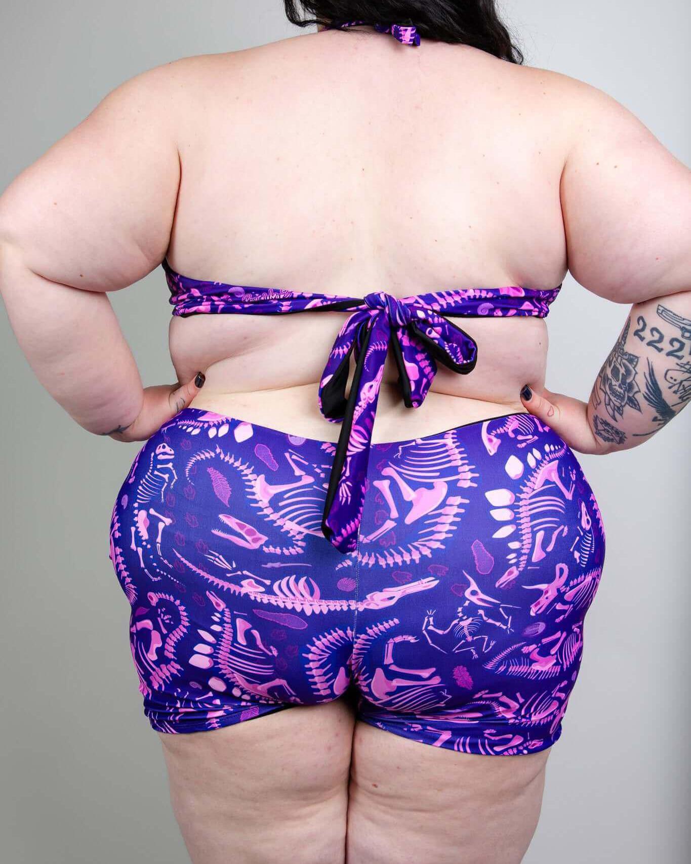 Back view of a plus-size model wearing a purple and pink dinosaur print bikini set, showcasing a playful summer style.