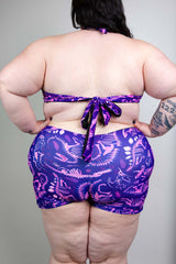 Model wearing Freedom Rave Wear romper with a purple dinosaur print, shown from the back, ideal for stylish rave outfits.