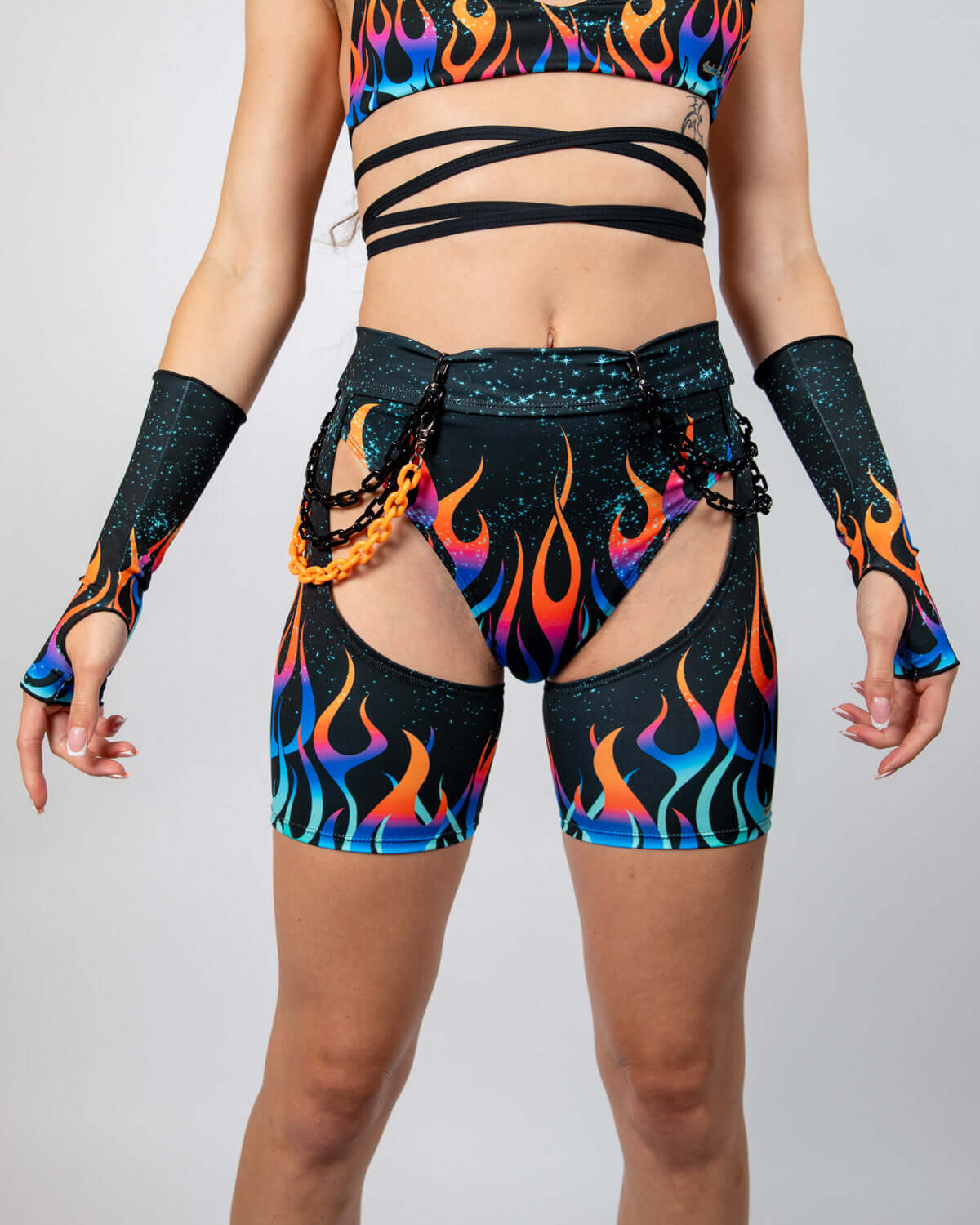 Model wearing Blaze Chaps with flame graphics, high-waisted fit, and attached chains, perfect for rave outfits.