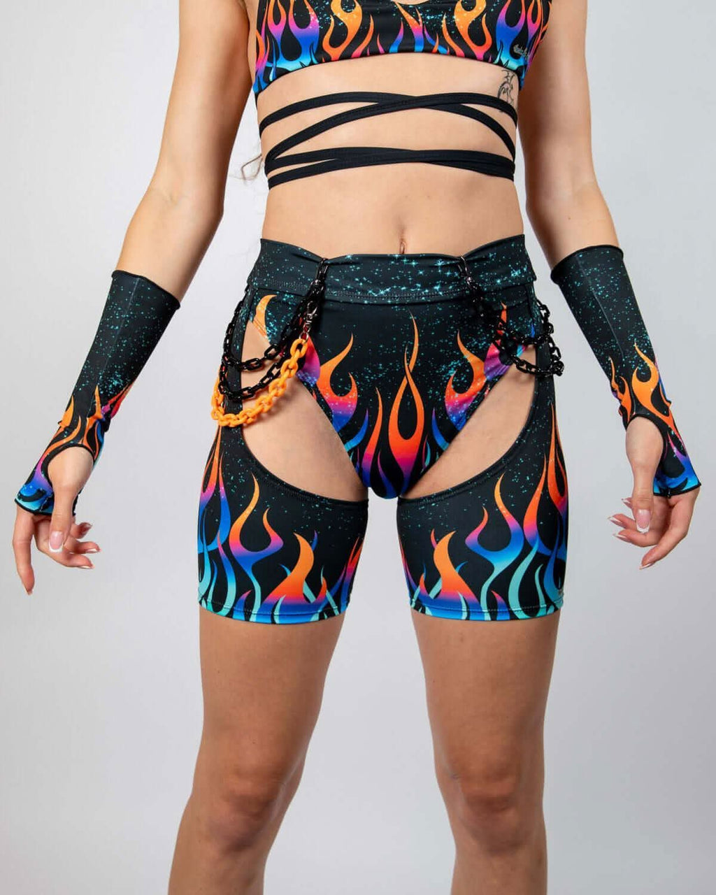 Model wearing Blaze Chaps with flame graphics, high-waisted fit, and attached chains, perfect for rave outfits.